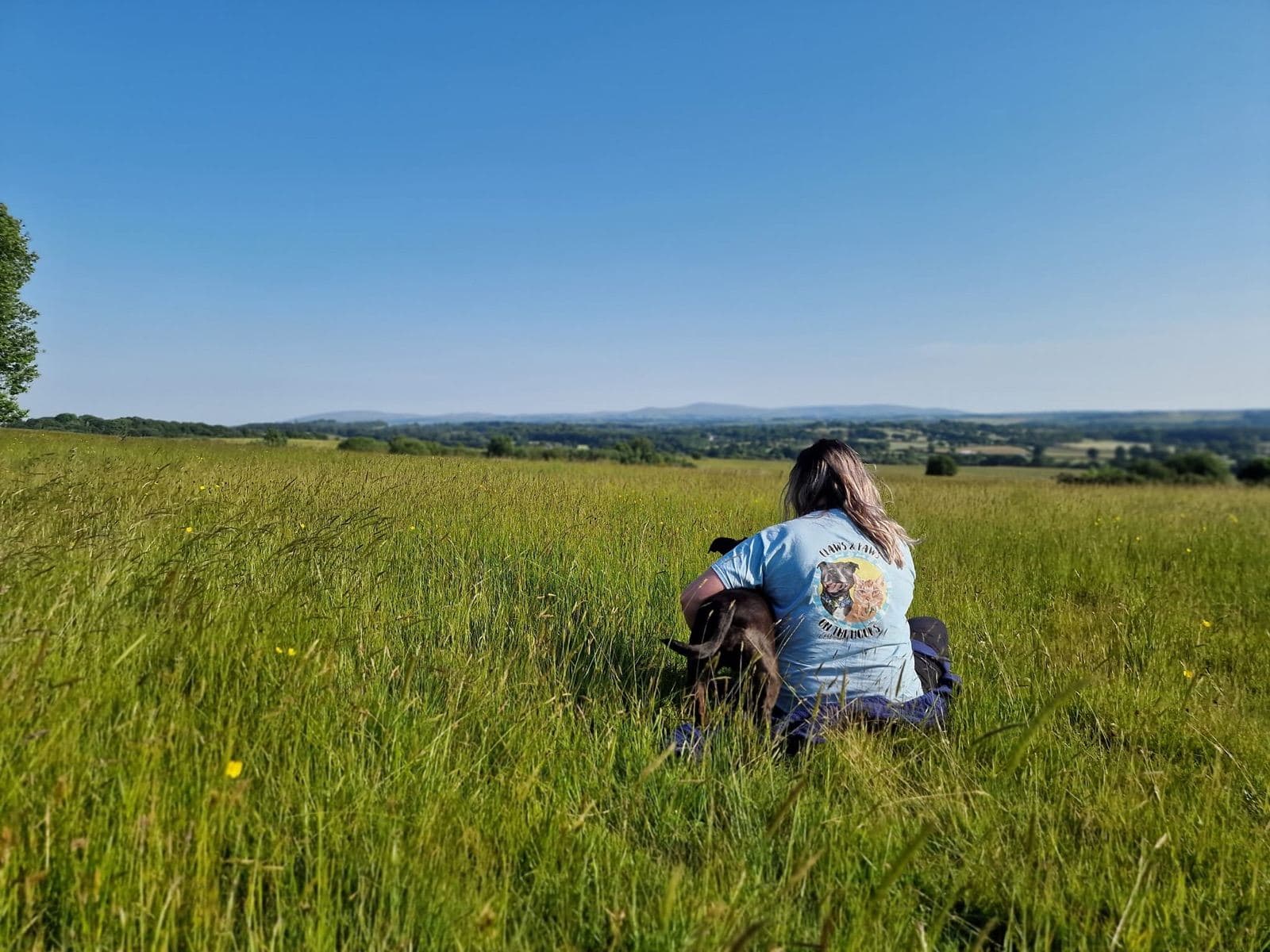Mel sat in a field hugging a dog under a big Dartmoor sky